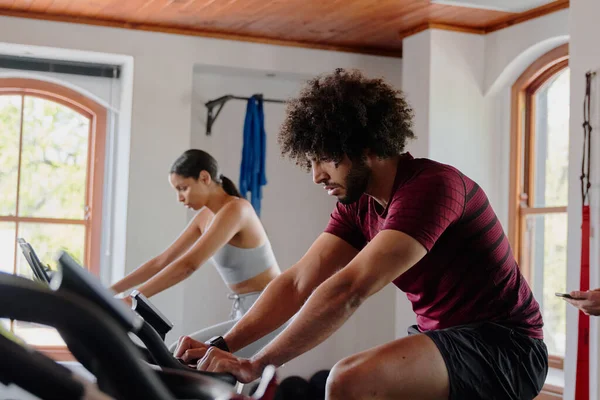 Young middle eastern man and biracial woman in sportswear cycling on exercise bike at the gym