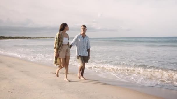 幸せな若いカップル笑顔と手を取りながらビーチを歩く — ストック動画