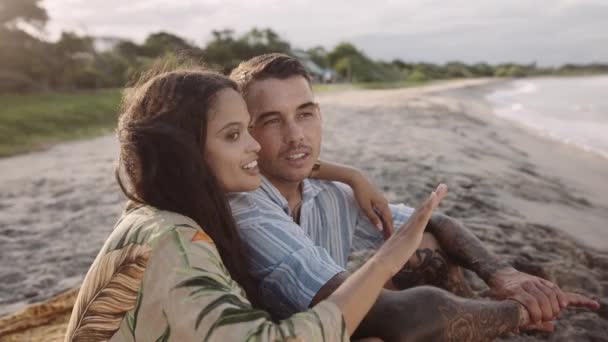 幸せな若いカップル座って話とジェスチャーオンビーチによって海 — ストック動画