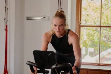 Spor giyim sektöründe odaklanmış beyaz bir kadın spor salonunda egzersiz bisikletinde kardiyo yapıyor.