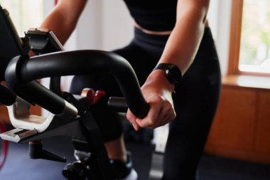 Spor kıyafetli beyaz bir kadının spor salonunda egzersiz bisikletiyle kardiyo yaptığı yakın çekim.