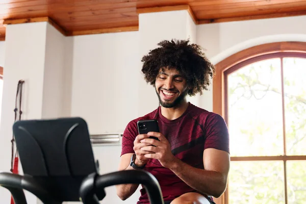 Giovane Uomo Mediorientale Abbigliamento Sportivo Utilizzando Telefono Cellulare Cyclette Palestra — Foto Stock