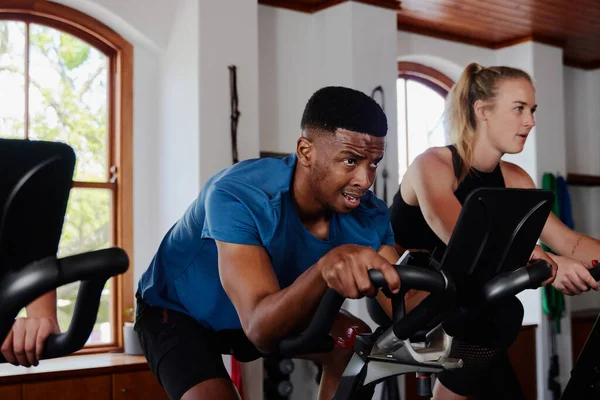 Determined young black man and caucasian woman in sportswear doing cardio on exercise bike at the gym