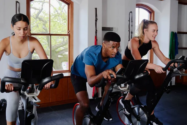 Group of determined young multiracial adults in sportswear doing cardio on exercise bike at the gym