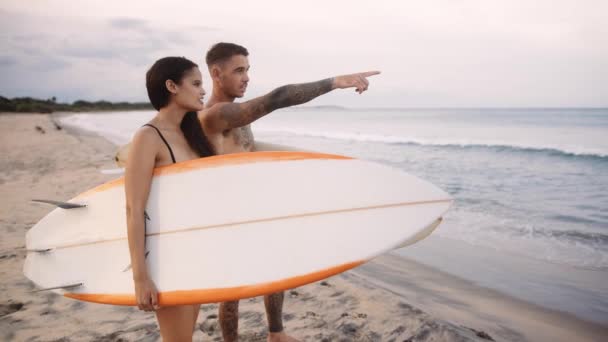 Unga Par Badkläder Som Bär Surfbrädor Medan Pekar Och Går — Stockvideo