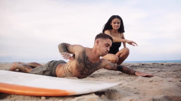 若いですBiracial女性教えボーイフレンドで水着どのようにパドルによってサーフボード上のビーチ — ストック動画