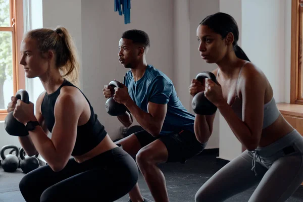 Três Jovens Adultos Multirraciais Focados Sportswear Fazendo Kettlebell Agachamentos Ginásio — Fotografia de Stock