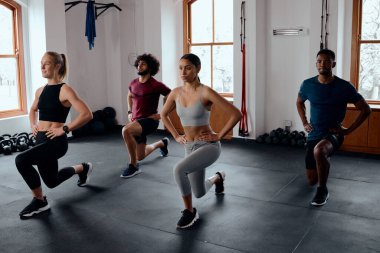 Spor giyim kuşamında bir grup çok ırklı genç yetişkin spor salonunda ellerinin kalçalarında hareket ediyorlar.