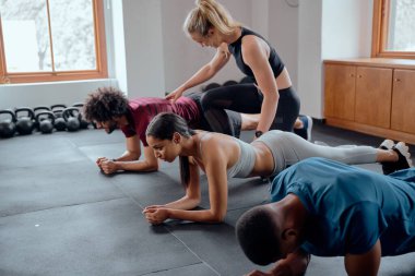 Spor giyim kuşamında spor giysileri giyen ve spor salonunda tahta egzersizleri yapan çok ırklı genç yetişkinlere yardım eden antrenör.