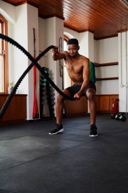 Gömleksiz genç siyah adam, spor salonunda gergin halat egzersizleri yaparken terliyor.
