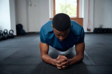 Spor kıyafetli kararlı genç bir zenci spor salonunda elleri bağlı kalas egzersizleri yapıyor.