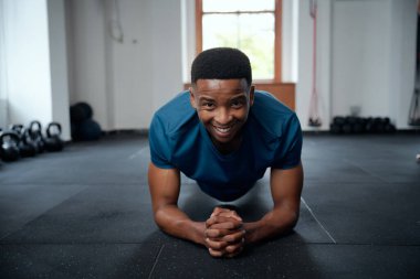 Spor kıyafetleriyle spor salonunda tahta egzersizleri yapan kendinden emin genç bir zenci portresi.