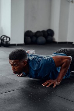 Spor kıyafetli kararlı genç bir zenci spor salonunda şınav çekiyor.