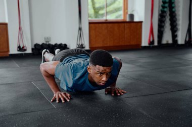 Spor kıyafetli genç bir zenci spor salonunda şınav çekiyor.