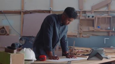 Dijital tablet üzerine dijital kalemle ahşap fabrikasında yazan çok ırklı genç adam.
