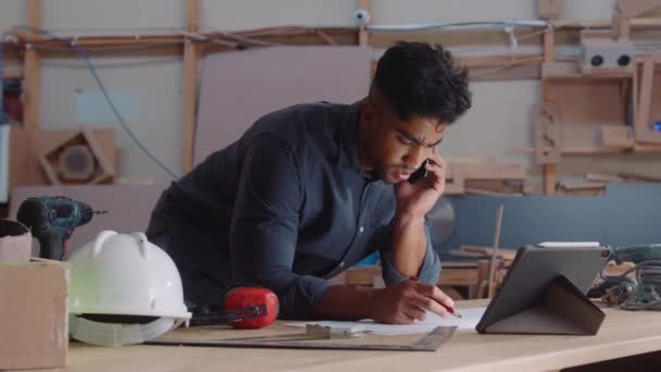 Wielorasowy Młodzieniec Rozmawiający Klientem Przez Telefon Komórkowy Podczas Pracy Stolarni — Wideo stockowe
