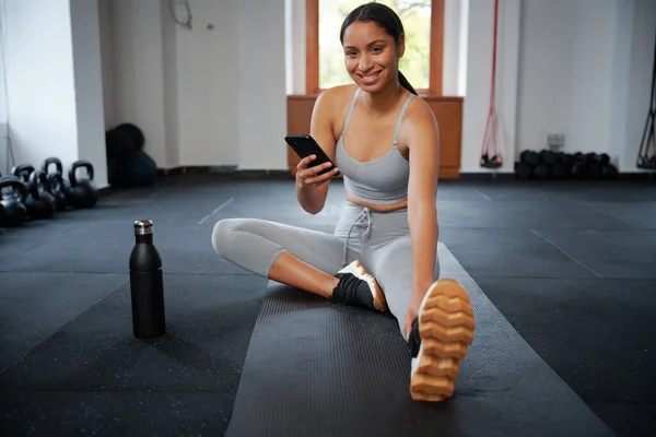 Ung Biracial Kvinna Sportkläder Mobiltelefon Medan Stretching Träningsmatta Gymmet — Stockfoto