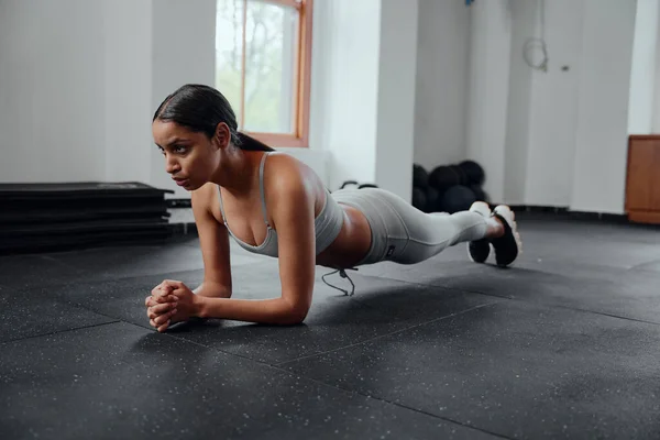 Determined young biracial woman in sportswear doing plank exercises at the gym