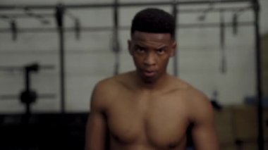 Spor salonunda kollarını kavuşturmuş kameraya bakan kaslı genç bir adamın portresi.