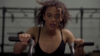 Spor giyimli, kararlı, çift ırklı genç bir kadın spor salonunda yoğun bir eliptik makine egzersizi yapıyor.