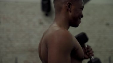 Azimli, üstsüz, kaslı, siyah bir adam spor salonunda halterle halter kaldırıyor.