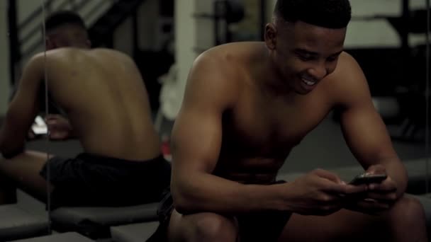 Shirtless Muskulös Ung Svart Man Ler När Använder Mobiltelefon Genom — Stockvideo
