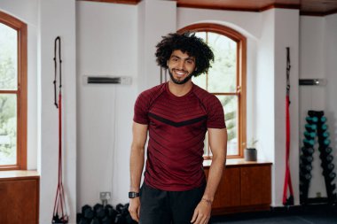 Spor giyim bölümünde spor salonundaki kameraya bakan mutlu orta doğulu bir genç.