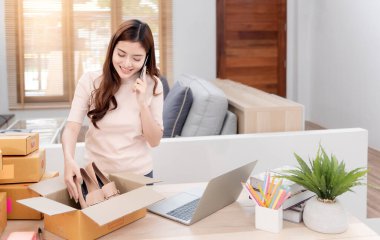Asyalı güzellik internetten dizüstü bilgisayarın siparişini kontrol ediyor. Ve mutlu bir gülümseme ile karton kutu paketleyin, yeni normal bir online iş olmak