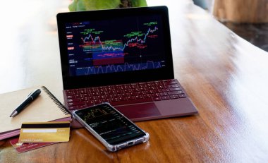 Ev üzerinden finansal hisse senedi grafiklerine yatırım yapmak ve bakmak için dizüstü bilgisayar ve akıllı telefon kullanma kavramı.