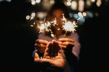 İnsan eli ve havai fişek soğuk bir ışık çubuğu. Parlak bokeh 'li, arka plan bulanık bir kadın.