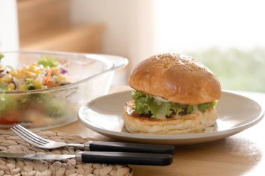 Hamburger beyaz tabakta ve sebze salatası ahşap masada