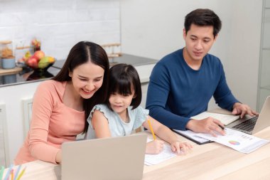 Güzel Asyalı kadınlar sevimli kızlara çevrimiçi çalışmayı öğretiyor ve yakışıklı erkekler evdeki masalarında dizüstü bilgisayar kullanarak çalışıyorlar. Bu aile için yeni bir normal hayat..