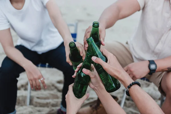 hands holding beverage bottles and touching each other at a party.