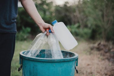 Bir adamın eli kullanılmış plastik şişeyi geri dönüşüm için çöp kutusuna atıyor..
