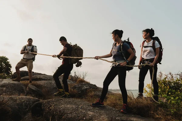 Bir grup erkek ve kadın turist dağlara tırmanmak için halat çeken dört Asyalı gezgin tırmanıyor..
