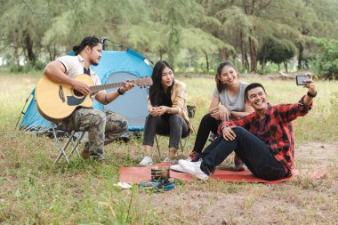 Dört Asyalı turist grubu ormanda akıllı telefonlarla selfie çekiyor.