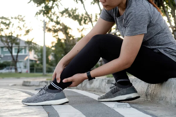 Spor kıyafetli Asyalı kadın ayak bileğini tutuyor..