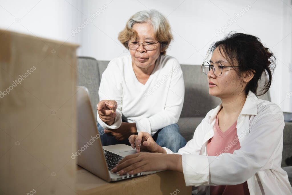 The concept of moving rooms and new houses, Asian teenage and elderly women, mother and daughter are chatting During the use of the laptop.