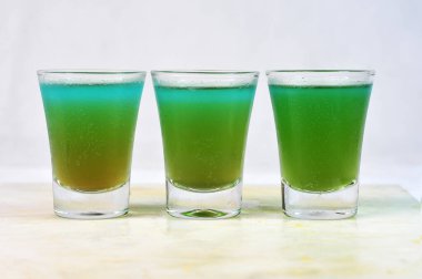 Üç doz absent, tekila ve votka masanın üstündeki cam bardakta limon, bulanık arka planda yatay görüntü.