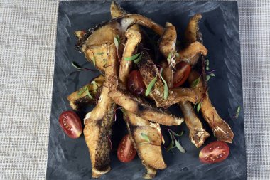 Beyaz arka planda taşın üstünde domatesli kızarmış balık şeritleri..