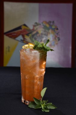 Böğürtlenli, buzlu ve cinle ferahlatıcı alkollü içecek, arka planda bulanık duran cam bardakta servis edilen limon kabuğu.