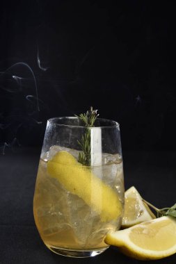 Böğürtlenli, buzlu ve cinle ferahlatıcı alkollü içecek, arka planda bulanık duran cam bardakta servis edilen limon kabuğu.