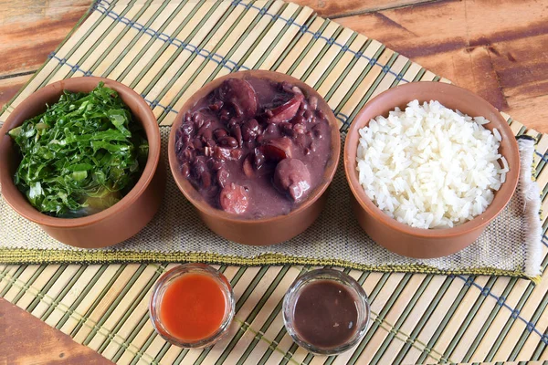Feijoada typical Brazilian food, beans with pork bacon, orange rice and flour, chili sauce and crackling