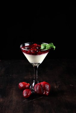 Beyaz çikolatalı dulce de leche ve ahududu ve çilek reçeli, ahşap bir masada bir bardakta servis edilir.