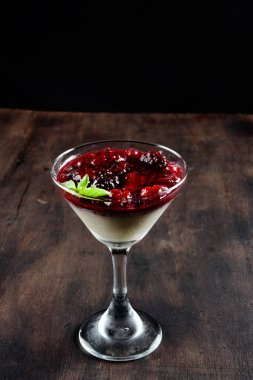 Beyaz çikolatalı dulce de leche ve ahududu ve çilek reçeli, ahşap bir masada bir bardakta servis edilir.