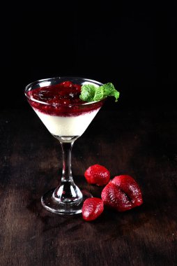 Beyaz çikolatalı dulce de leche ve ahududu ve çilek reçeli, ahşap bir masada bir bardakta servis edilir.