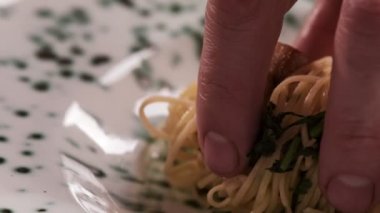 Çelik spagetti kaşığı kullanan bir aşçının yakın çekimi, pişirilmiş makarnayı bir restoranın mutfağında beyaz bir tabağa koyar. Mutfakta yemek pişirmek