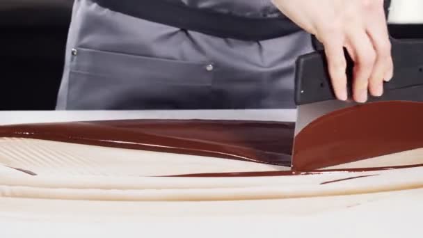 Čokoládové bonbóny. Žena kuchařka v uniformě temperování roztavené čokolády na bílém kamenném stole pomocí škrabku a pyrometru. — Stock video