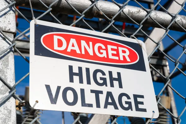 Danger High Voltage sign on chain link fence with power generators in the background.
