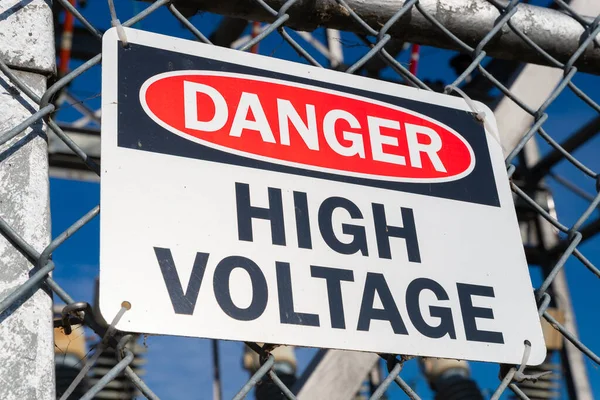 Danger High Voltage sign on chain link fence with power generators in the background.